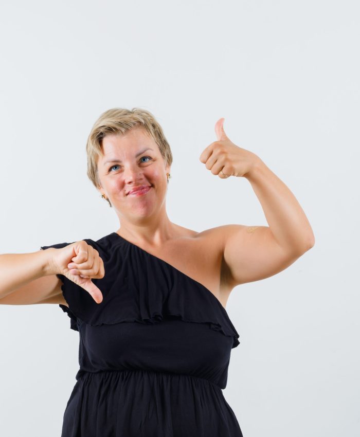 beautiful woman in menopause showing thumb up and down in black blouse and looking hesitant , front view.